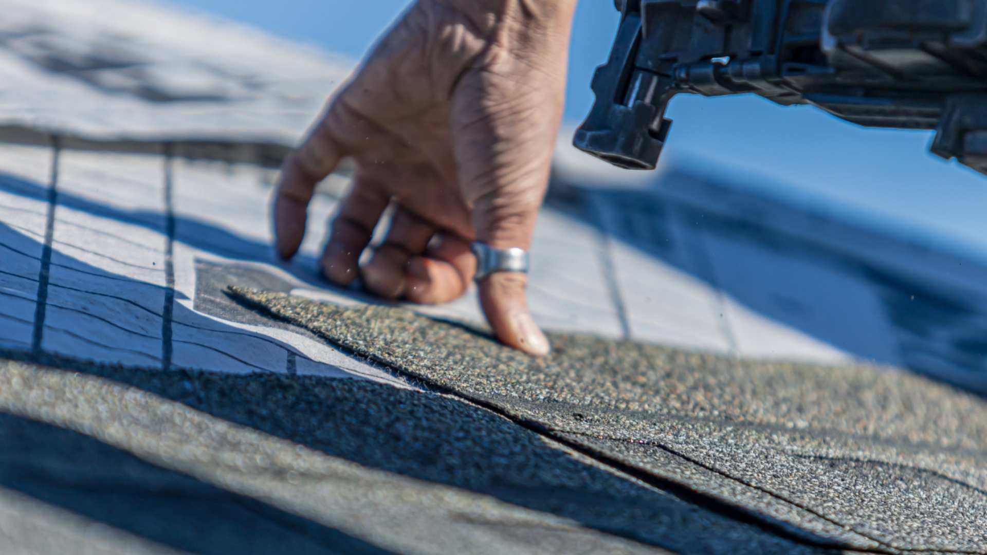 Trade nailing shingle into roof with nail gun. 
