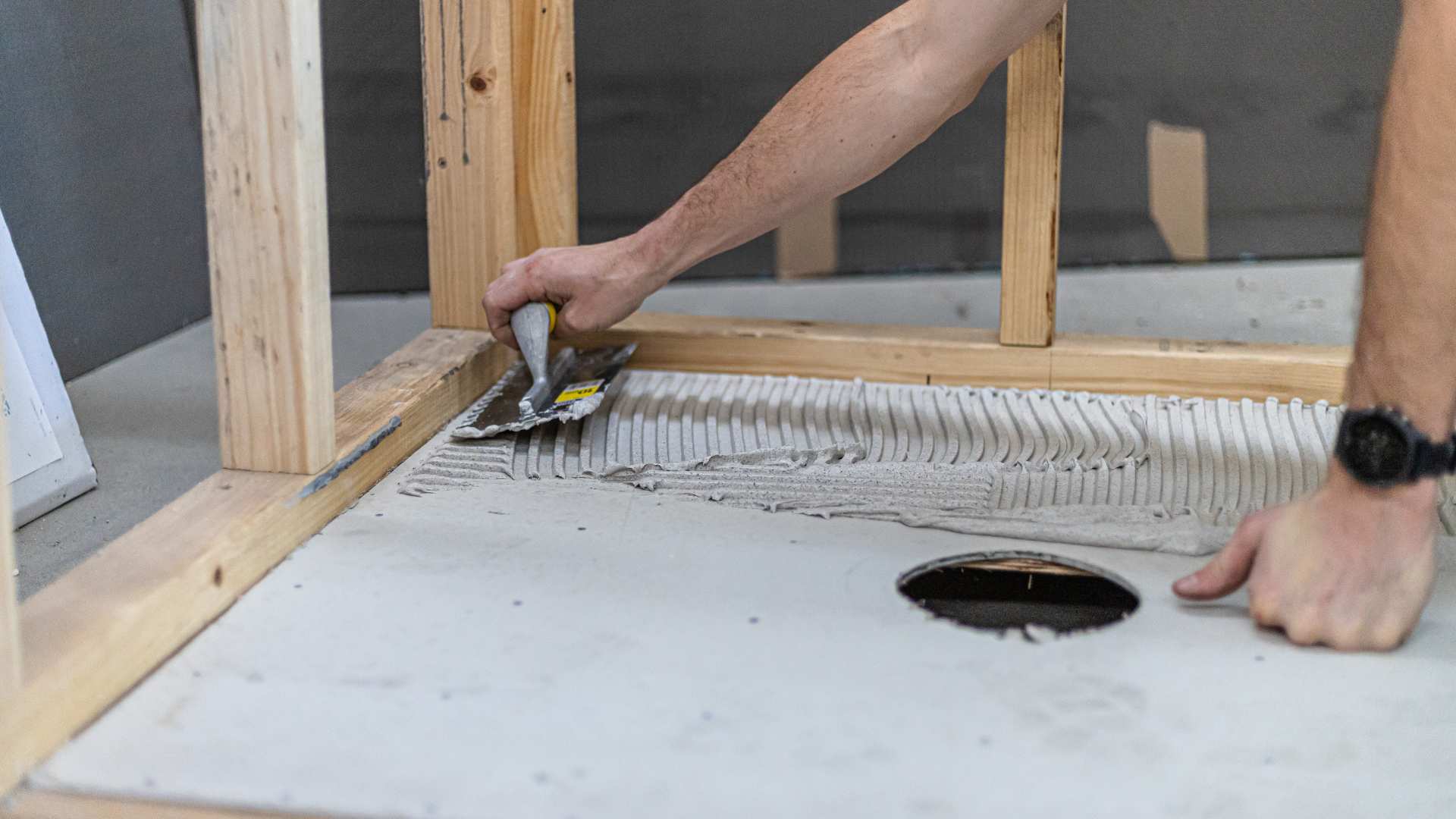 Application of adhesive using a trowel on bathroom floor.