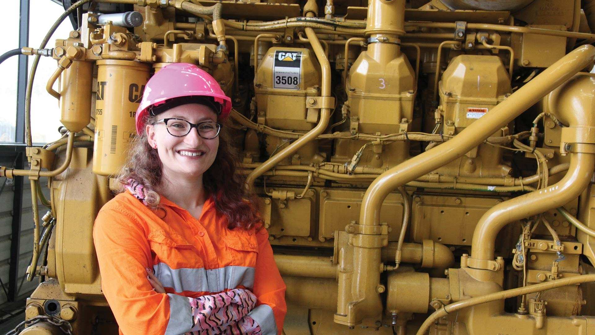 Louise Azzopardi smiling in front of machinery with hardhat.