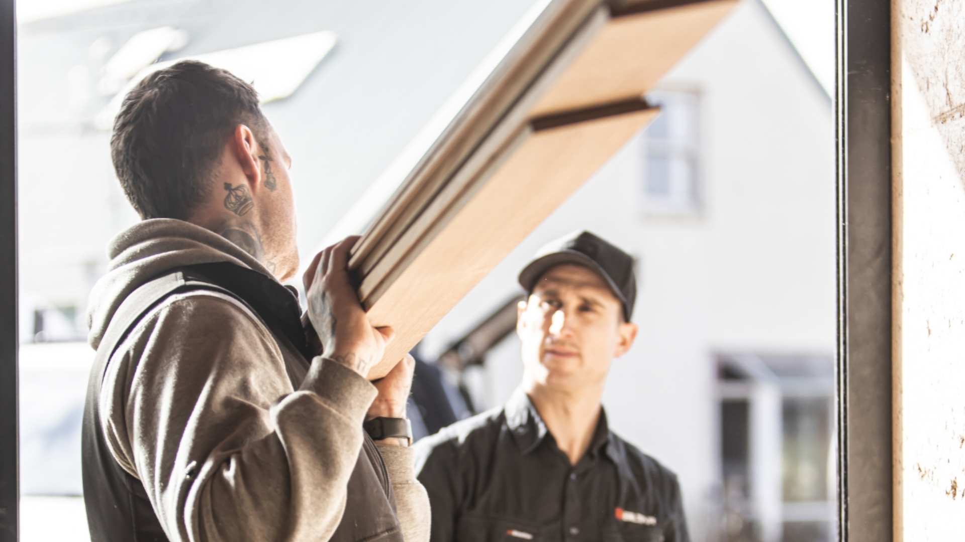 Builders talking as one is carrying two timber planks. 