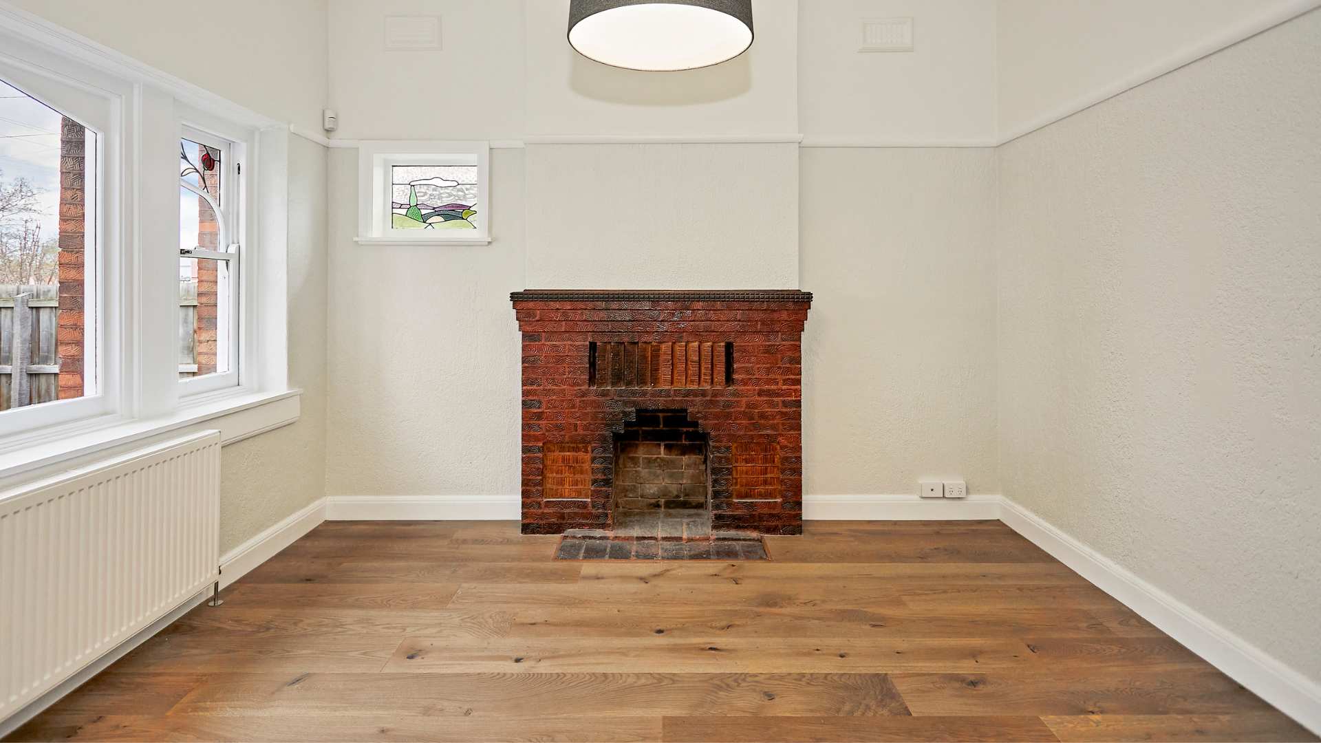 A brick fireplace in an empty room with timber flooring.