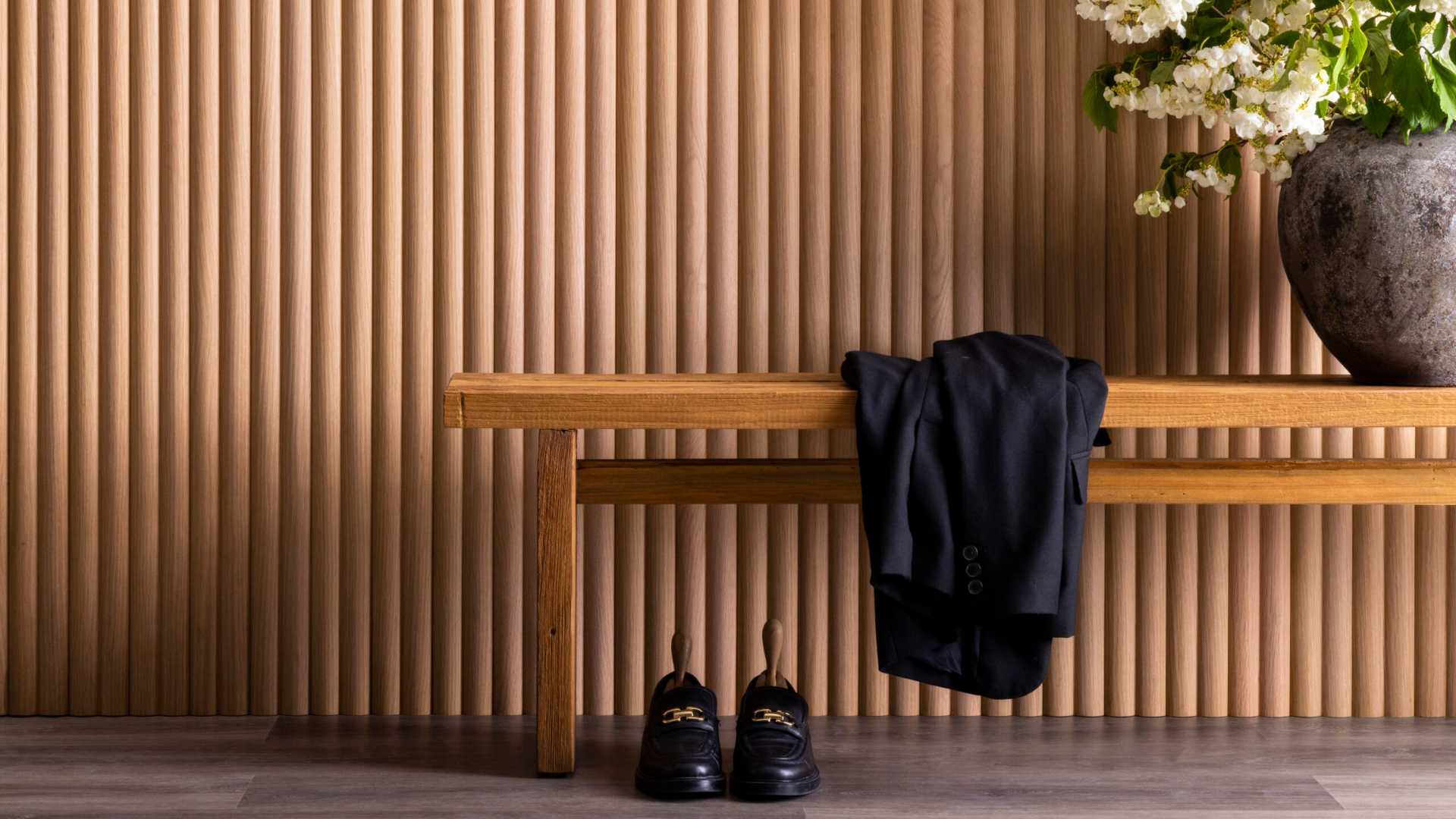 Interior wall lined with wooden bench, shoes, and vase of flowers.