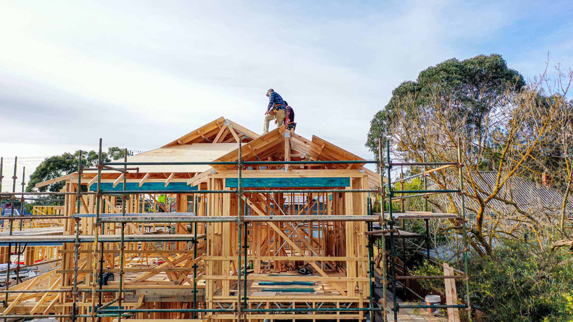 Framing timber structure of house with trades continuing the building process.