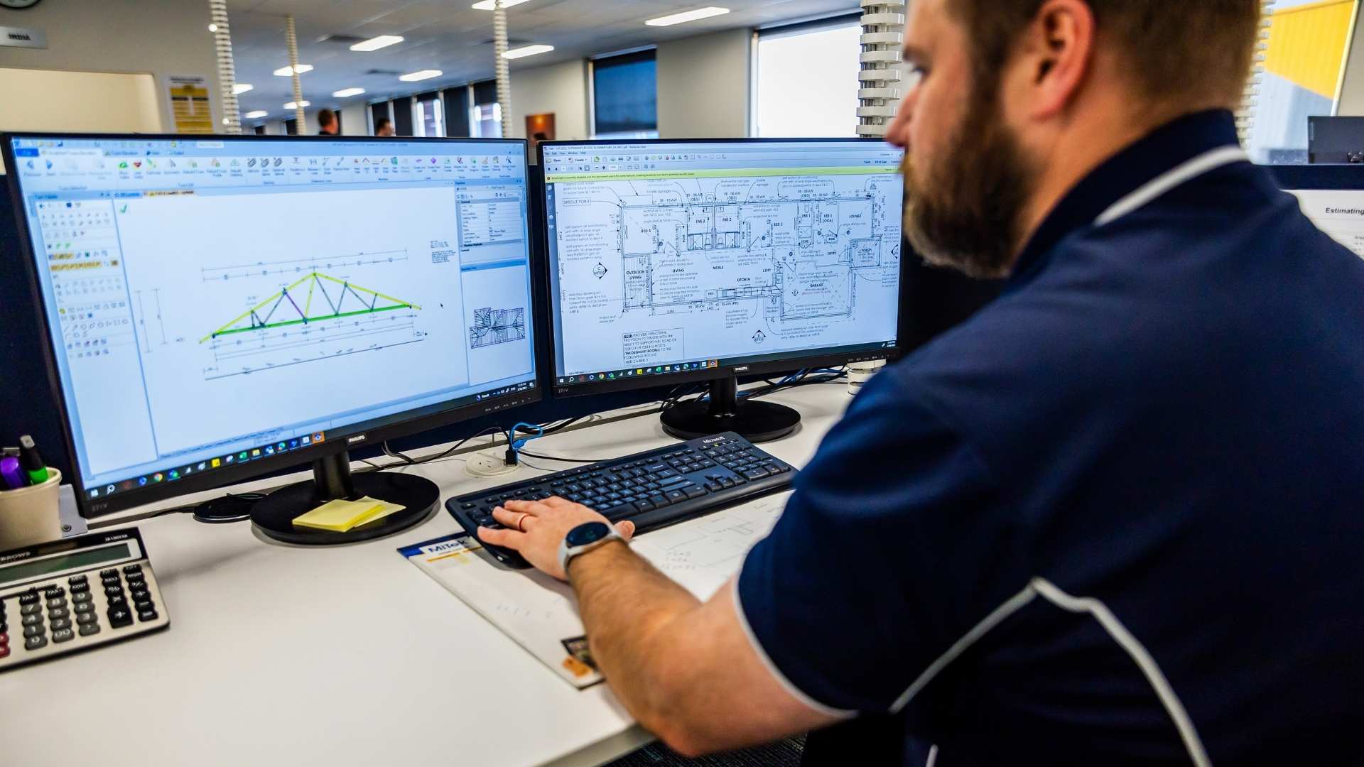 Man at desk looking at technical drawings of timber trusses.