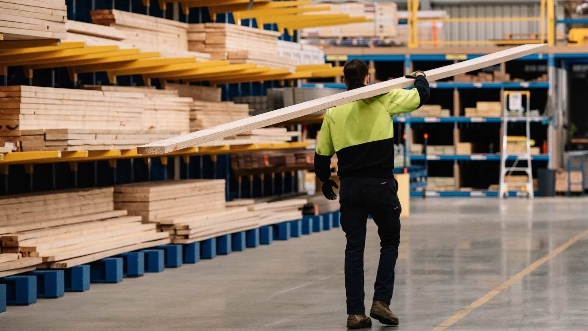 Yardie walking with plank of timber through yard.