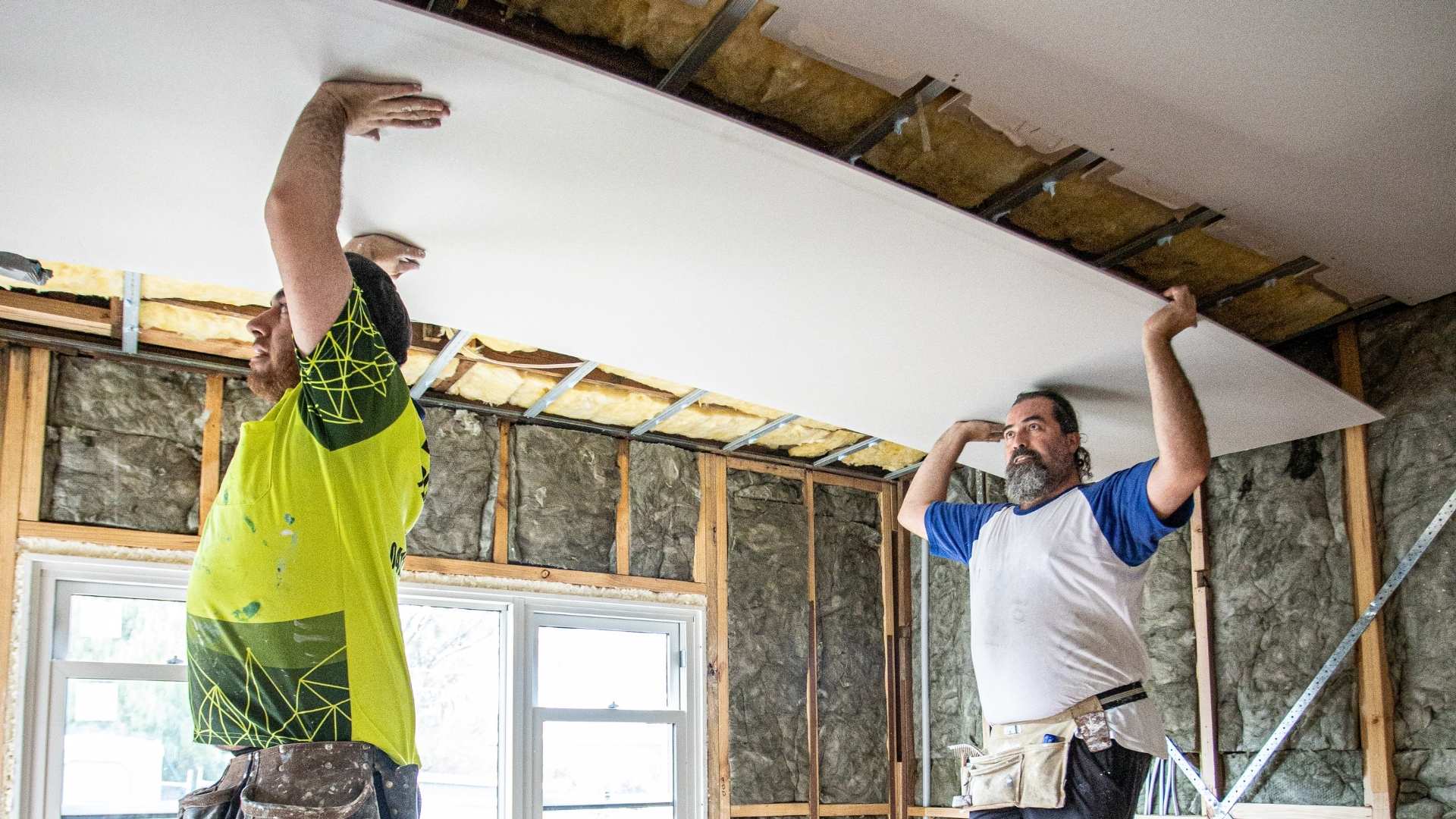 Two trades installing plasterboard into ceiling.