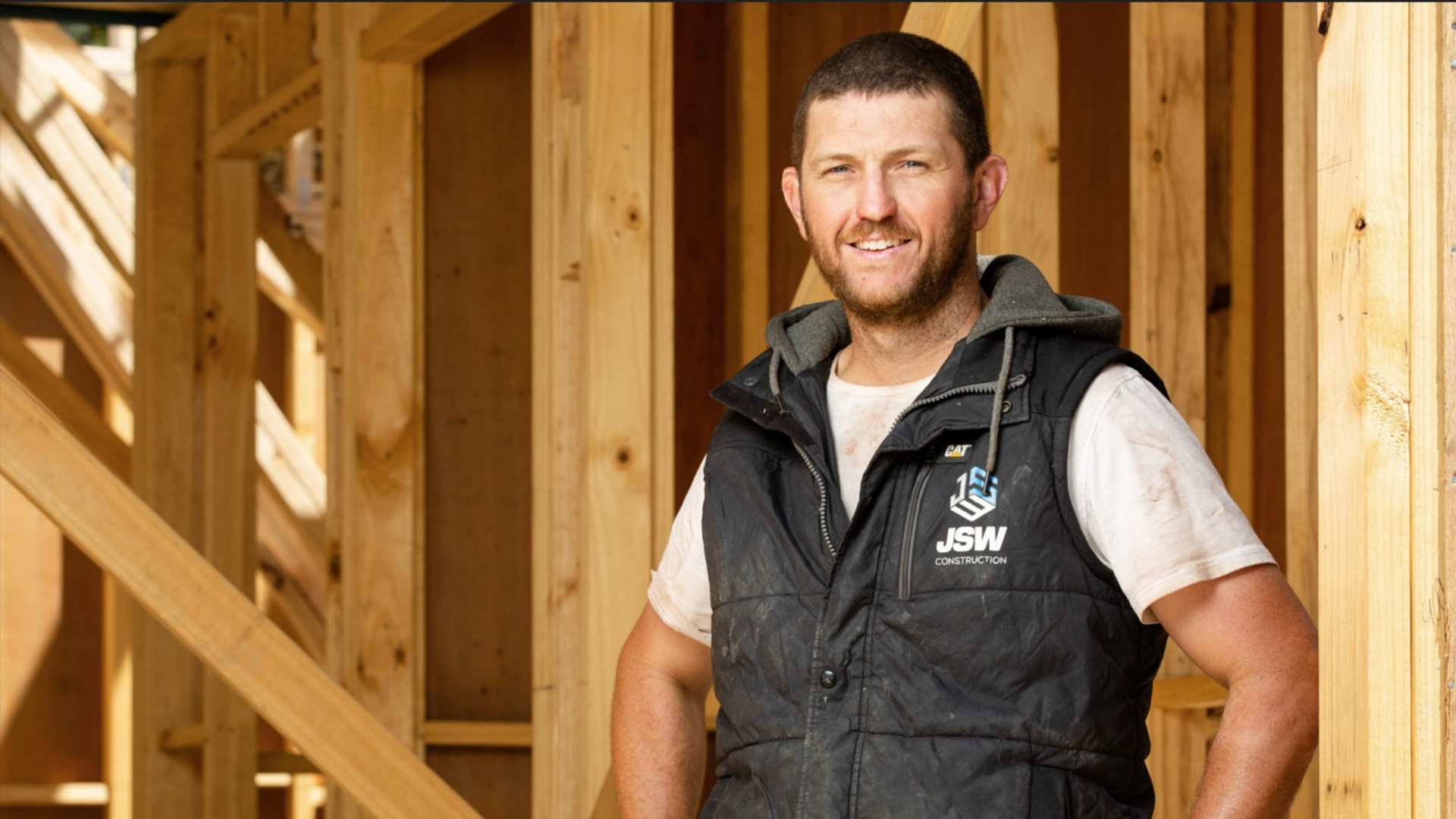 Trade smiling at camera amongst timber framing.