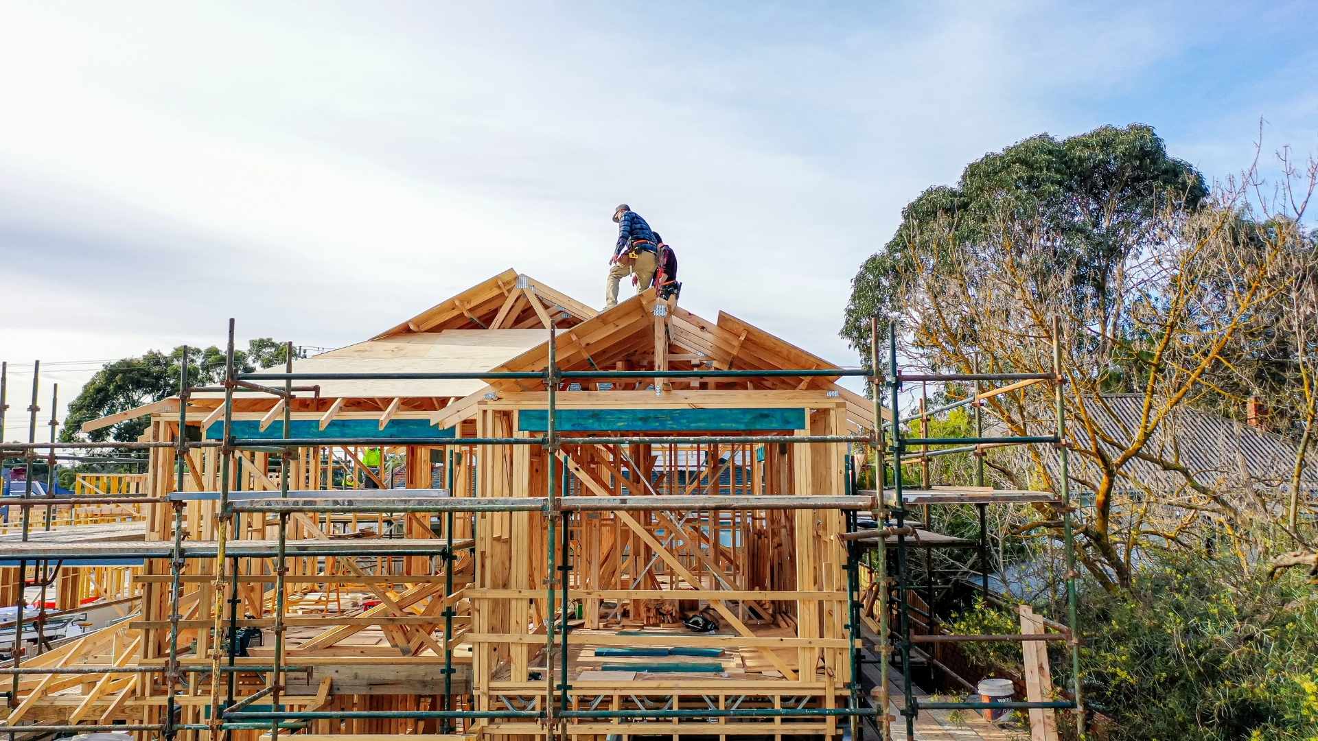 Two builders on roof of house during the framing stage.